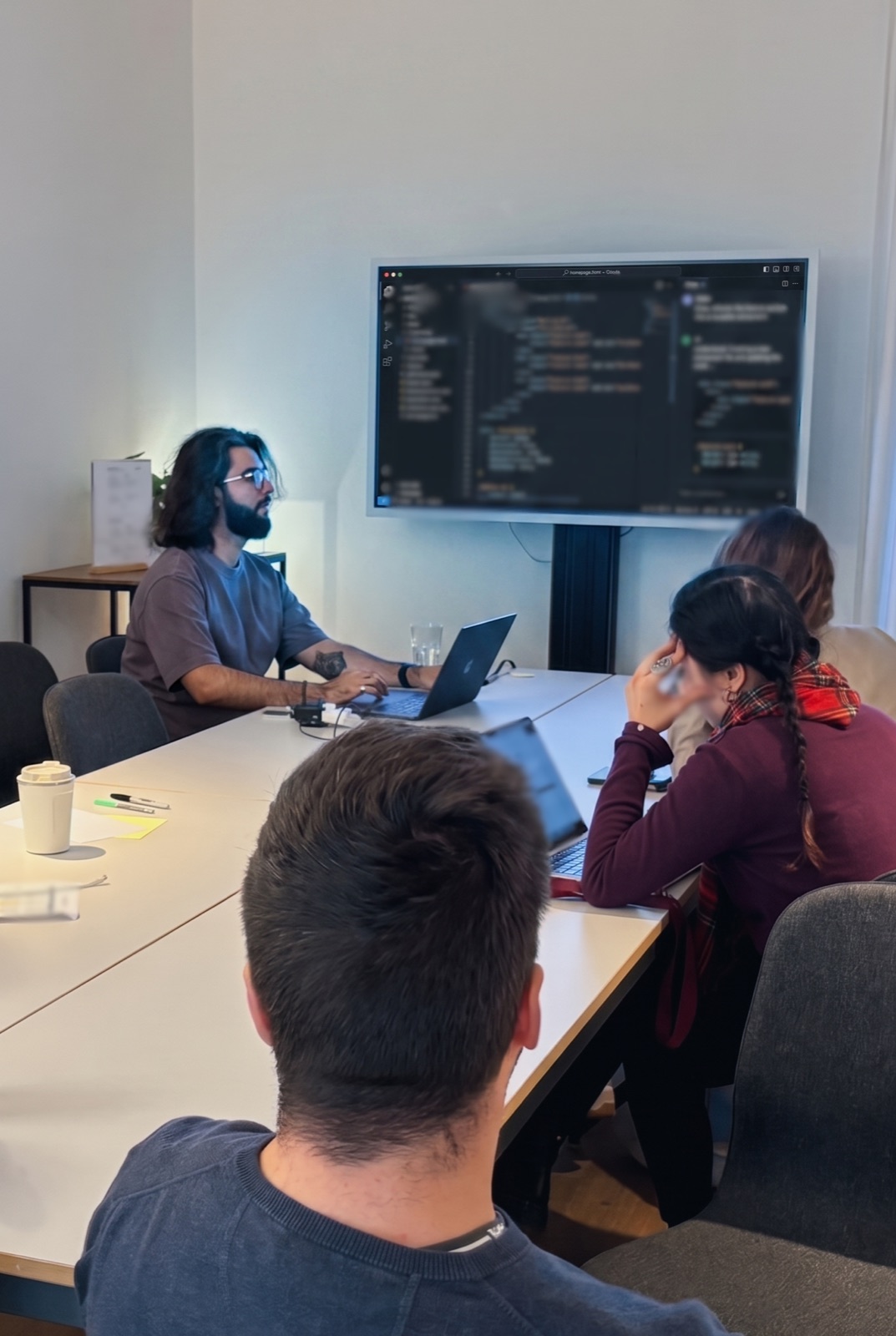 Saman demonstrating AI-assisted coding to fellow founders at the ChangemakerXchange AI Fellowship in Berlin, with VSCode and the Cline extension visible on a large screen.